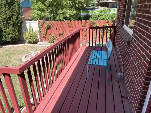Wood deck with painted railings, brick exterior, and a fenced yard with mature landscaping