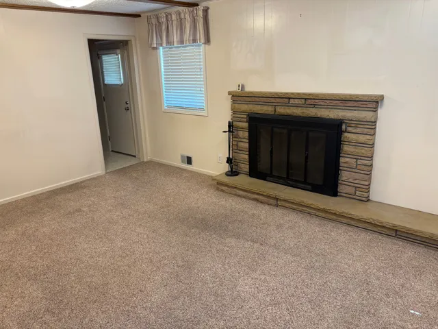 Stone-clad fireplace with a hearth, wall-to-wall carpeting, and a window with blinds