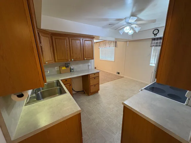 Wood-finish cabinetry, double basin stainless steel sink, light-toned countertops, and a built-in electric stovetop