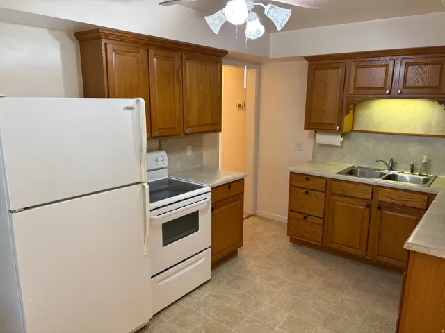 Kitchen featuring wood cabinetry, laminate countertops, a double basin stainless steel sink, and tile flooring