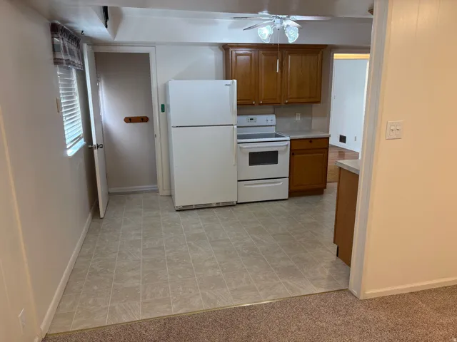 Kitchen area featuring a ceiling fan, wood-finish cabinetry, a white appliance suite, and tiled flooring