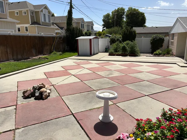 Paved patio with checkerboard design, defined grass border, wood fencing, and a storage shed