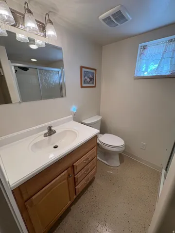 Vanity with integrated sink and chrome faucet, wood-finish cabinetry, wall-mounted mirror, and overhead vanity lighting