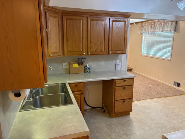 Kitchen featuring wood-finish cabinetry, a double basin stainless steel sink, and a light-toned countertop