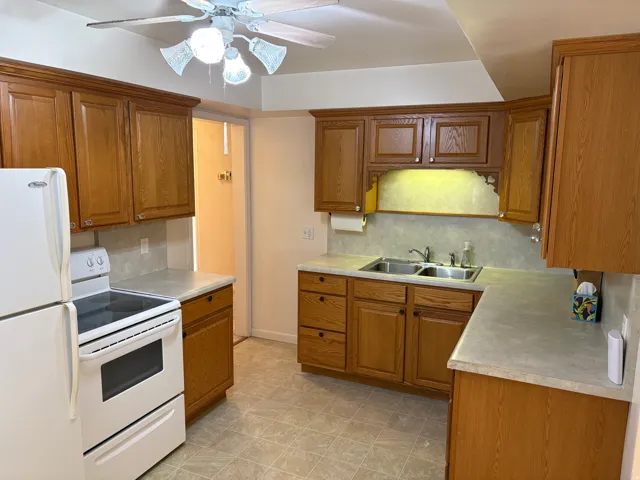 Kitchen featuring wood-finish cabinetry, white appliances, a double basin sink, and a ceiling fan with integrated lighting