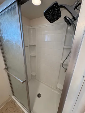 Enclosed shower with a textured glass door, white tile-patterned surround, and dual shower heads