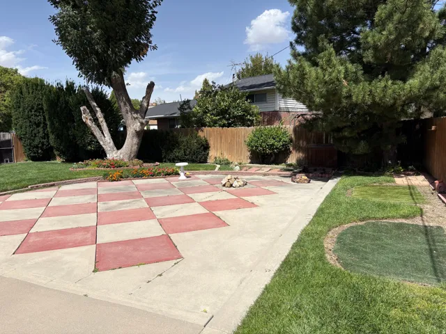 Expansive backyard featuring a checkerboard patio design, mature trees, manicured lawn, and a privacy fence