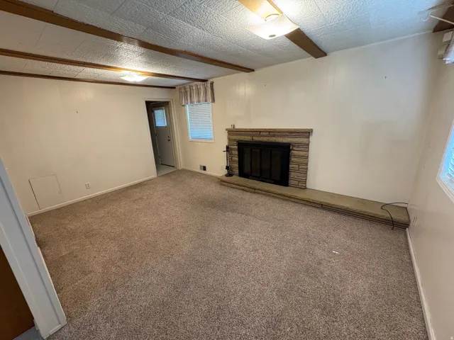 Spacious living area featuring a stone-clad fireplace with hearth, exposed wood beams, and textured ceiling