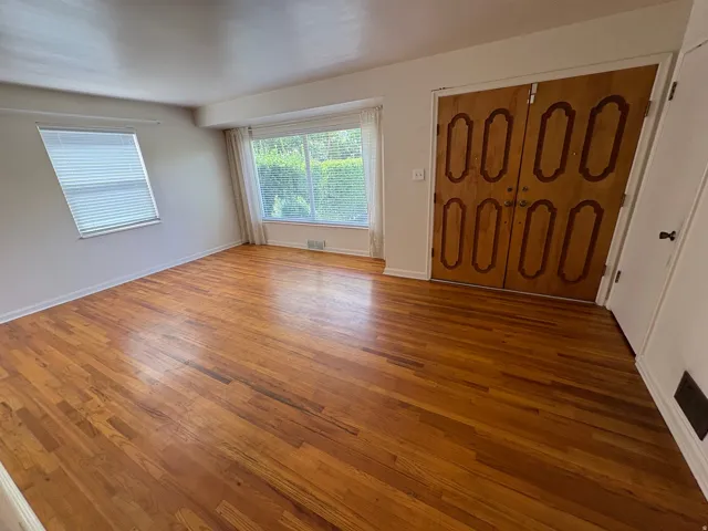 Hardwood flooring throughout, featuring a bay window, an additional window with blinds, and double entry doors with decorative paneling