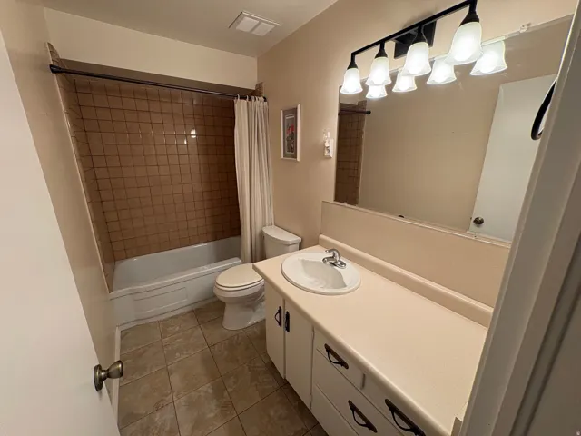 Ceramic tile flooring, vanity with integrated sink, full-width wall mirror, and a shower-over-tub combination with tile surround
