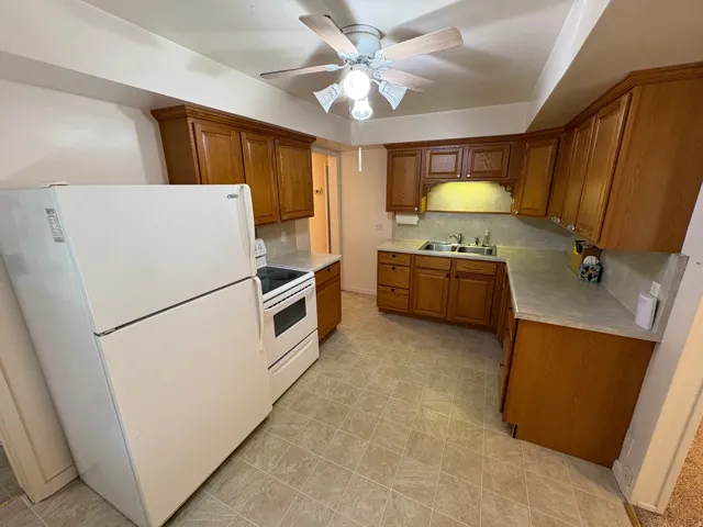 Kitchen featuring wood cabinetry, laminate countertops, a double basin sink, and a ceiling fan with integrated lighting