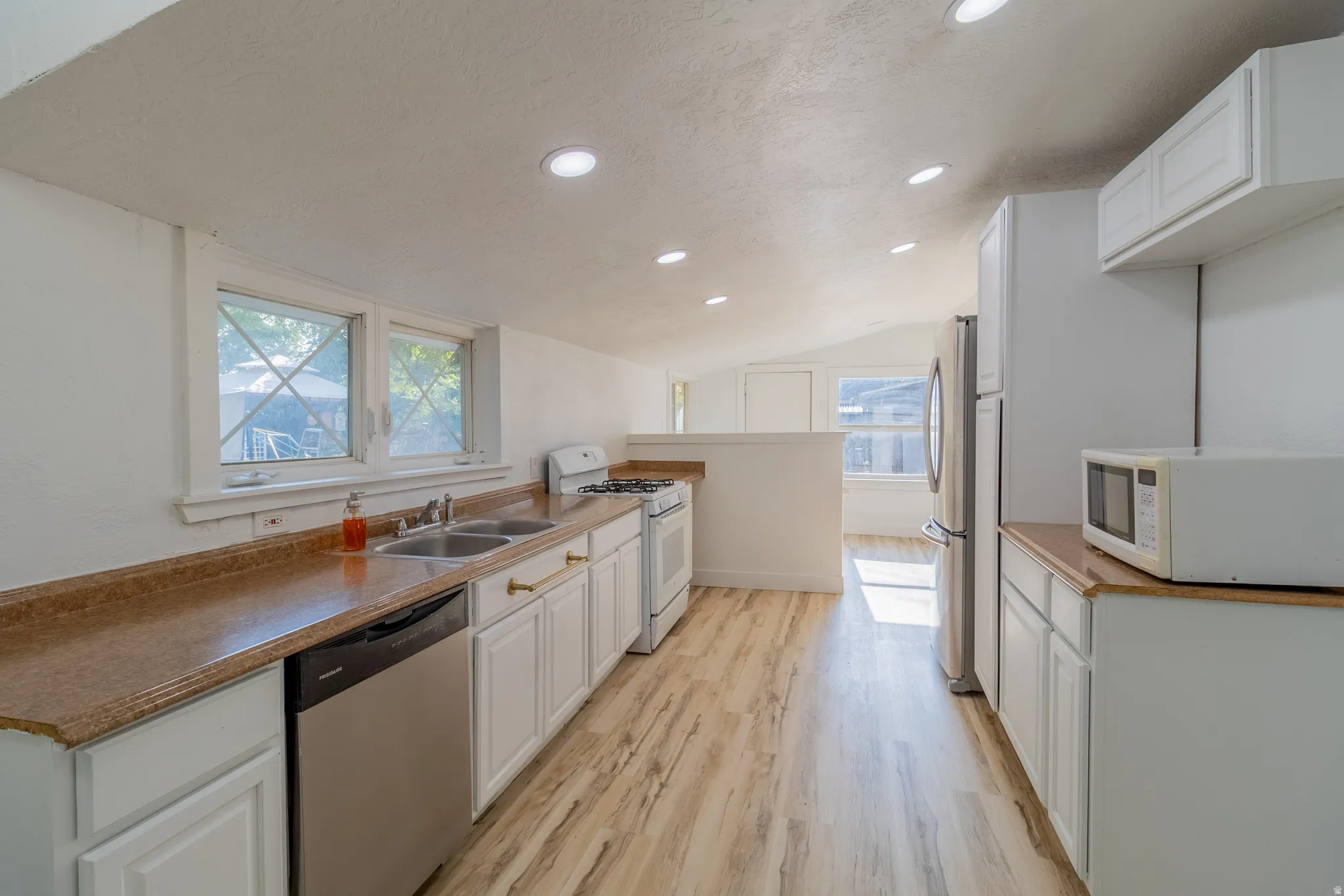Kitchen featuring wood-finish flooring, white cabinetry, a double basin sink, stainless steel appliances, and recessed lighting