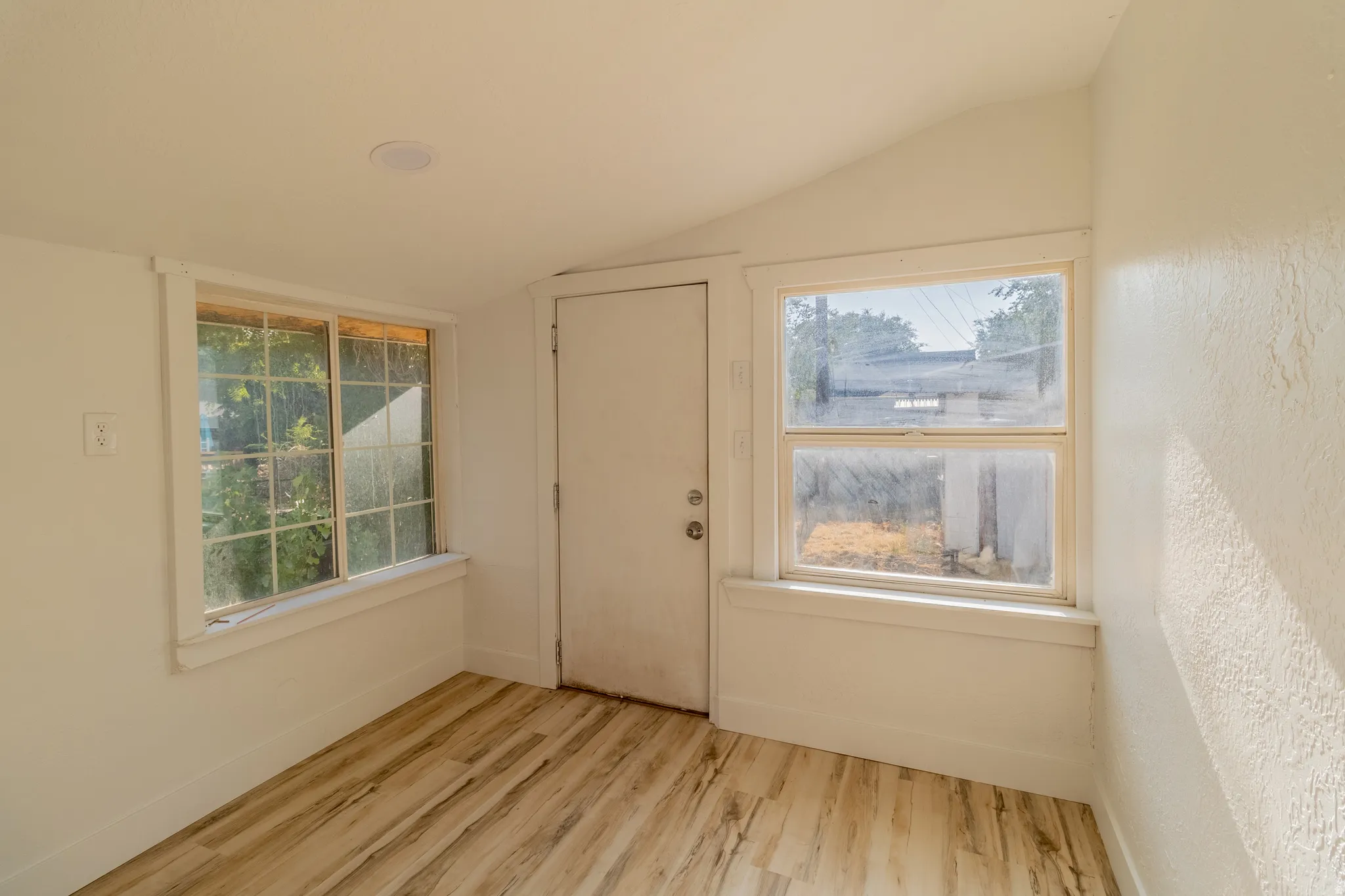 Wood-finish flooring, white painted walls, two windows with white trim, and a sloped ceiling with a recessed light