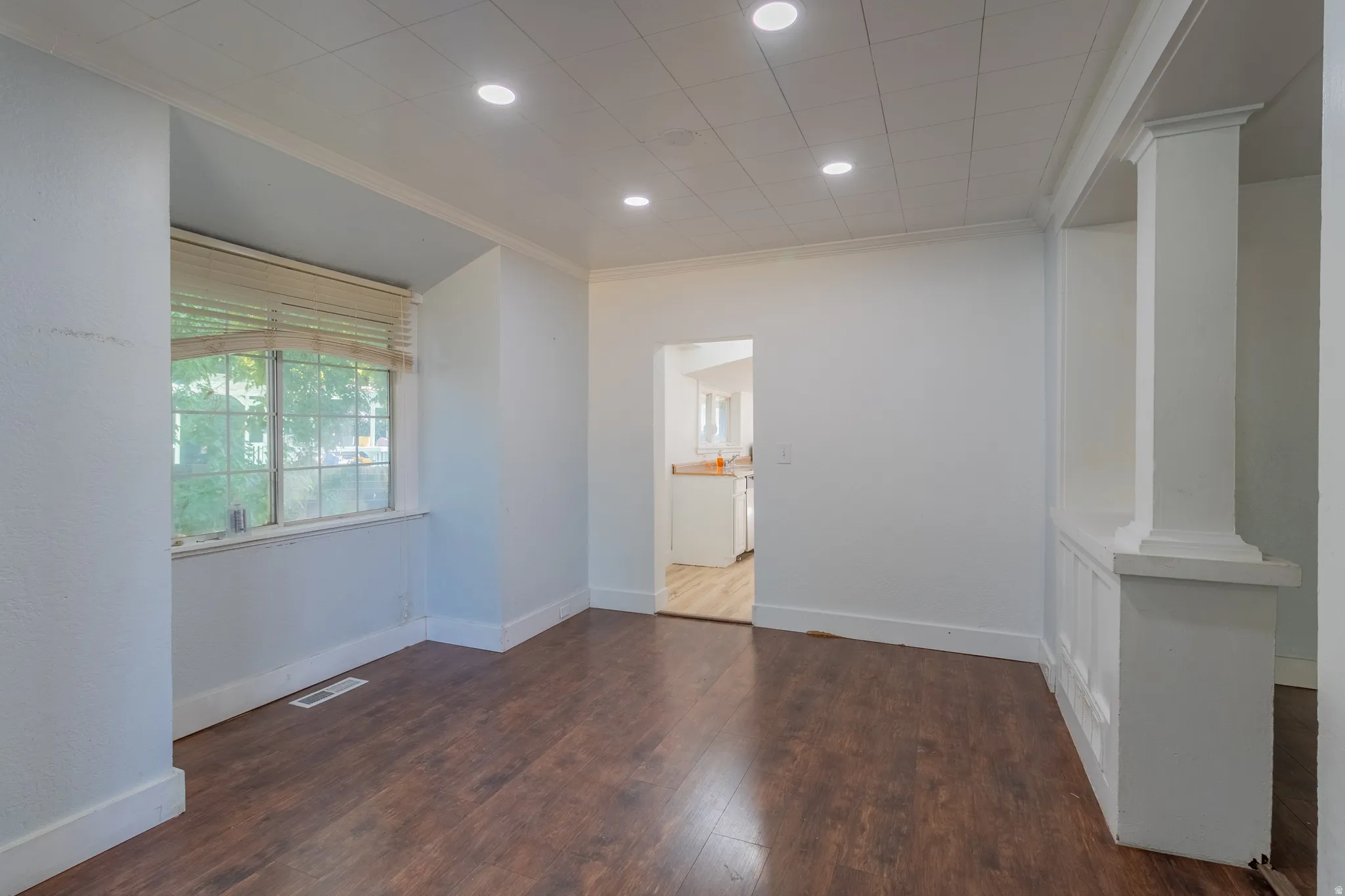Recessed ceiling lighting, crown molding, wood-finish flooring, interior architectural columns, and a large window