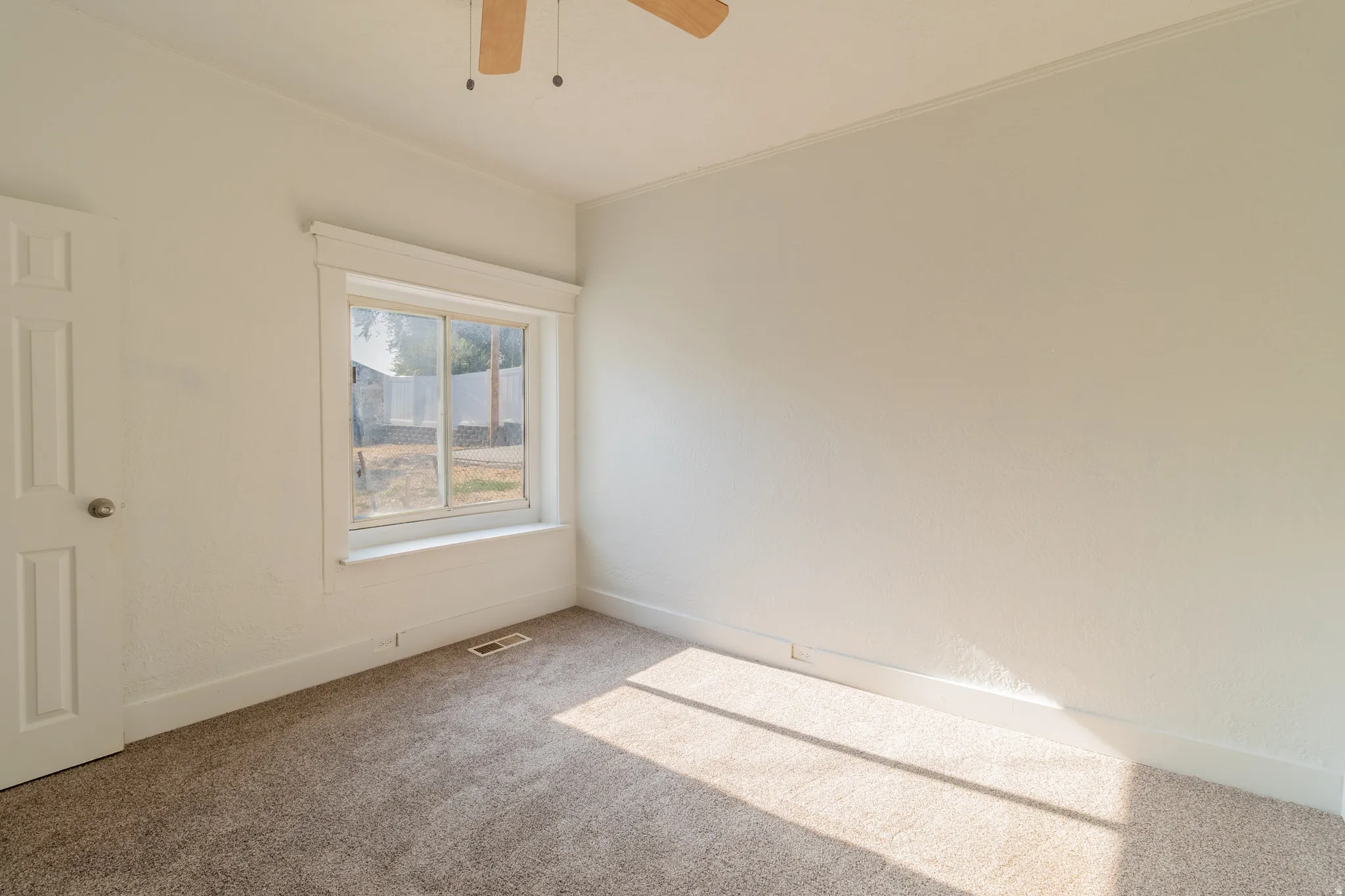 Carpeted flooring, white painted walls, window with white trim, white paneled door, and wood-finish ceiling fan