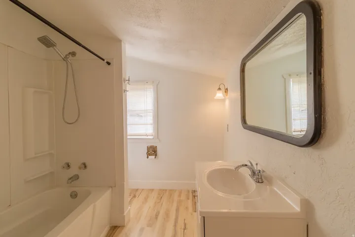 Bathroom featuring a white vanity with an integrated sink, chrome faucet, and wood-finish flooring