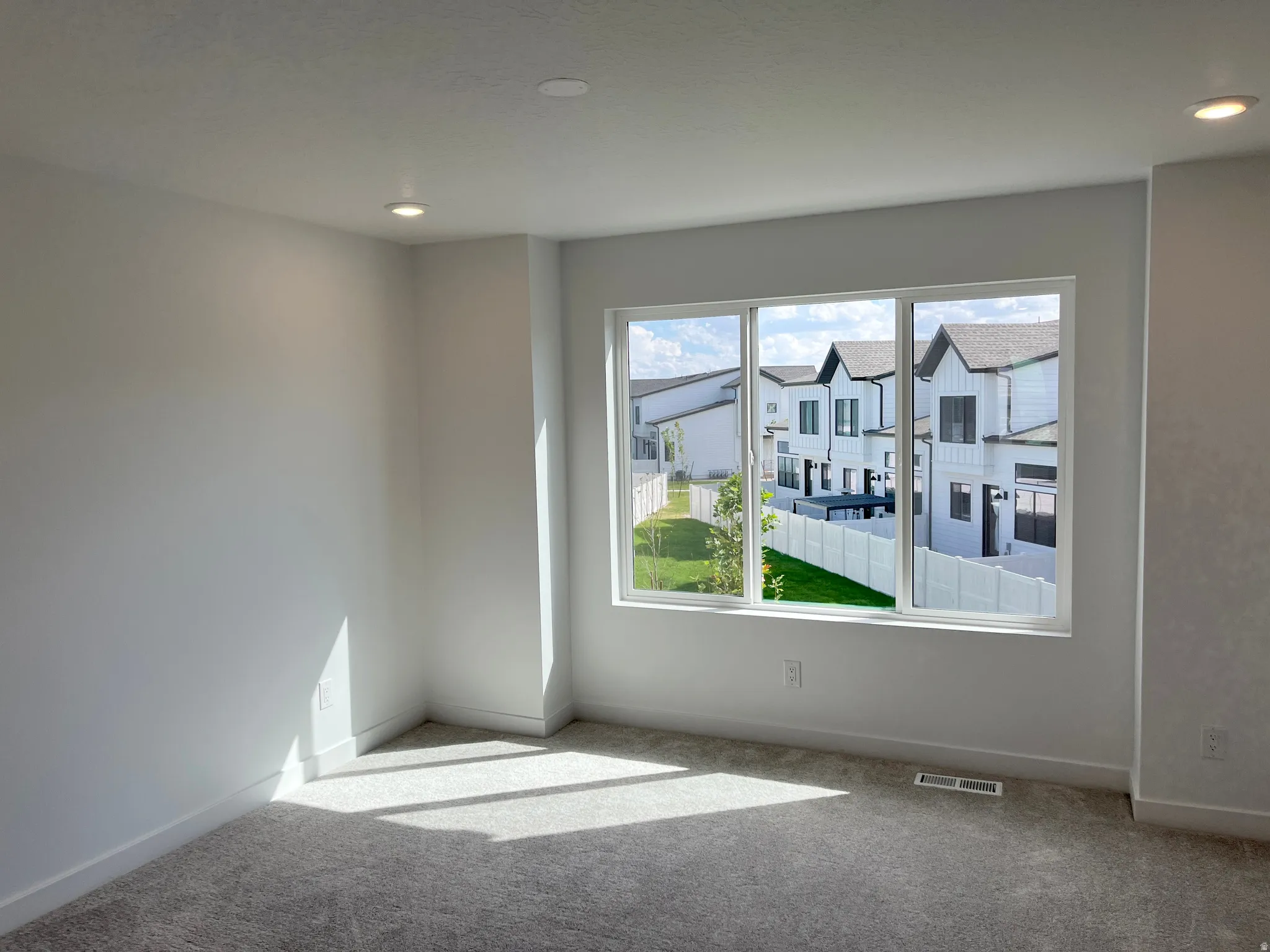 Recessed ceiling lighting, white interior walls, gray carpet flooring, and a multi-pane window
