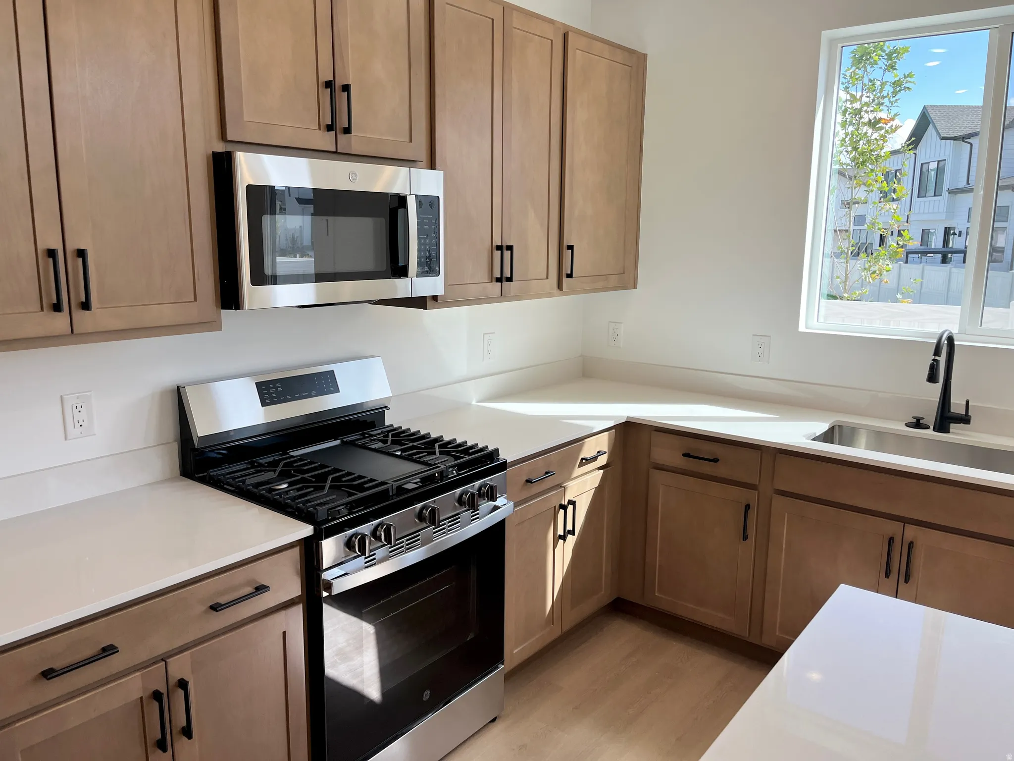 Full kitchen featuring wood-finish cabinetry, stainless steel appliances, light-toned countertops, and a stainless steel sink with a matte black faucet