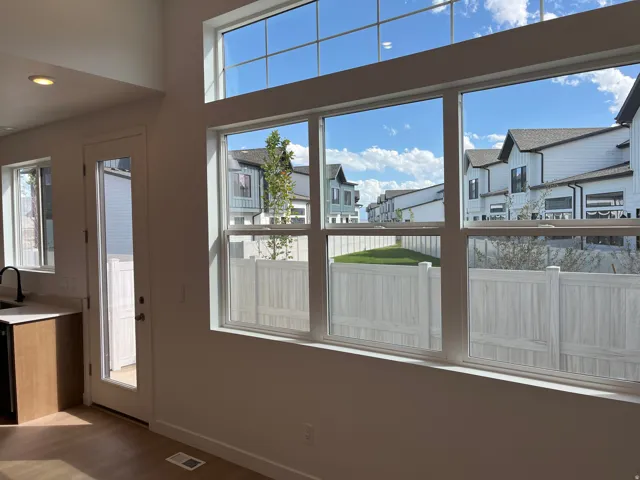 Large windows with transom elements, light wood-finish flooring, white walls, built-in cabinetry, and a white privacy fence