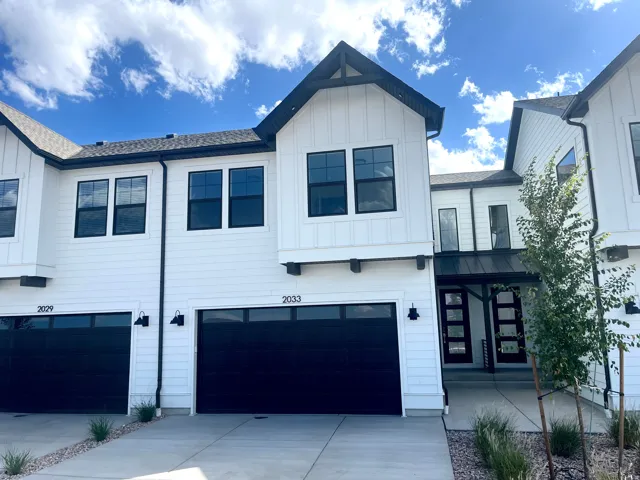 Modern farmhouse exterior with white vertical siding, black-framed windows, a black garage door, and a black metal entry awning