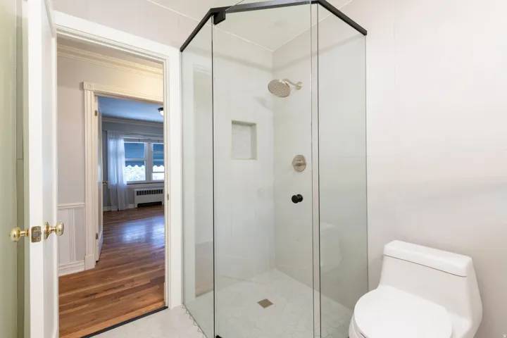 Glass-enclosed shower with a rainfall showerhead, brushed nickel fixtures, and a built-in shower niche