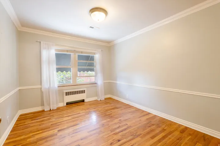 Hardwood flooring, painted walls, crown molding, chair rail molding, and a window with a radiator below