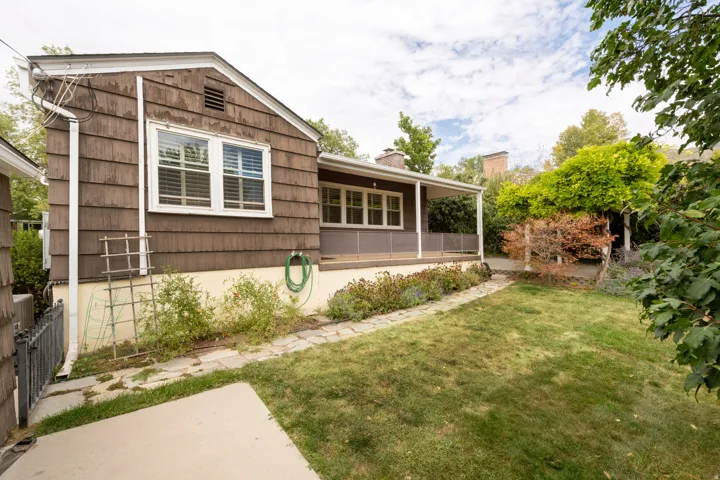 Gable-roofed residence with shingle siding, covered outdoor living space, and an expansive lawn