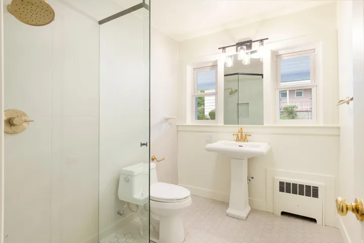 Bathroom featuring a glass-enclosed shower, rain shower head, pedestal sink, and hexagonal floor tiling