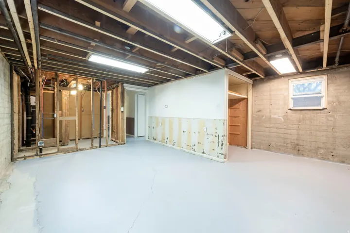 Exposed ceiling joists with visible utilities, concrete flooring, window, and framed partition walls with built-in shelving