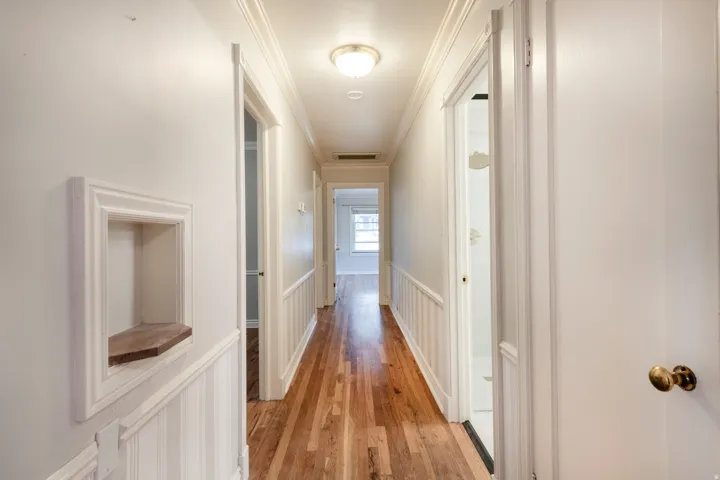 Hallway with wood-finish flooring, wainscoting, crown molding, and recessed wall niche with wood shelf
