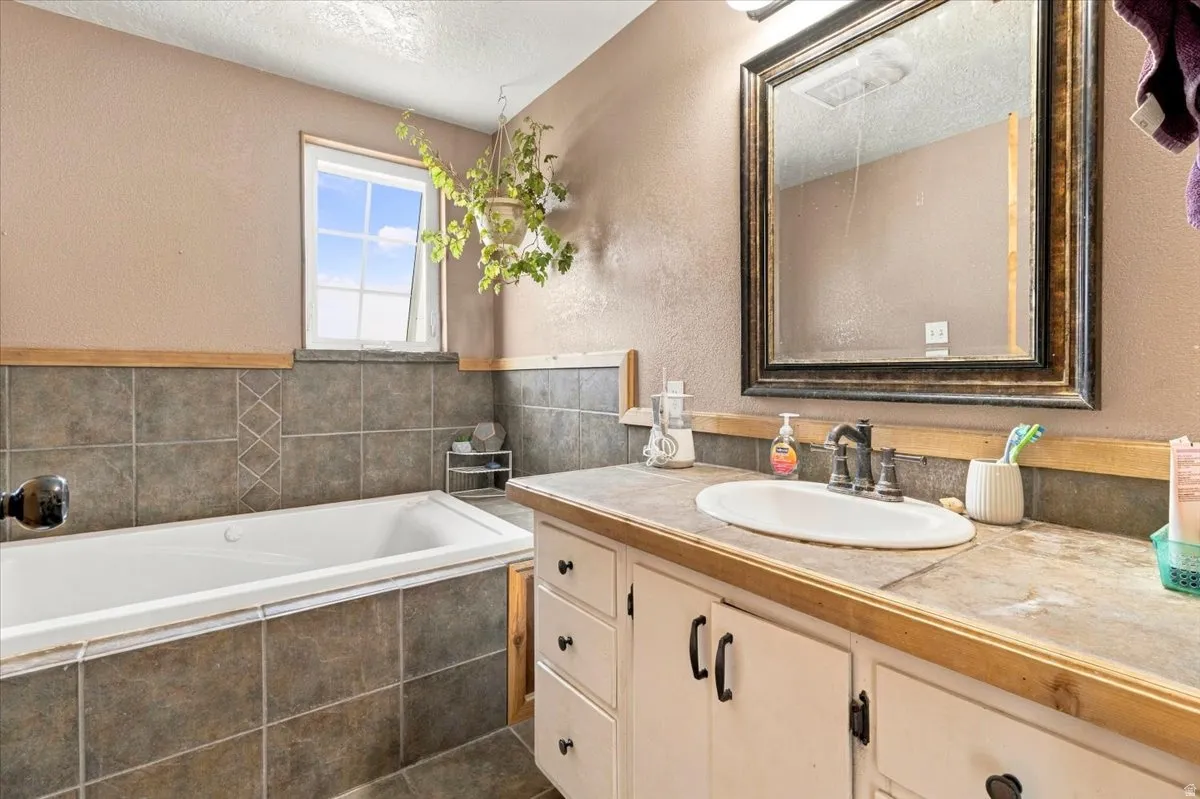 Built-in bathtub with surrounding tile, single vanity with integrated sink, framed mirror, and a window