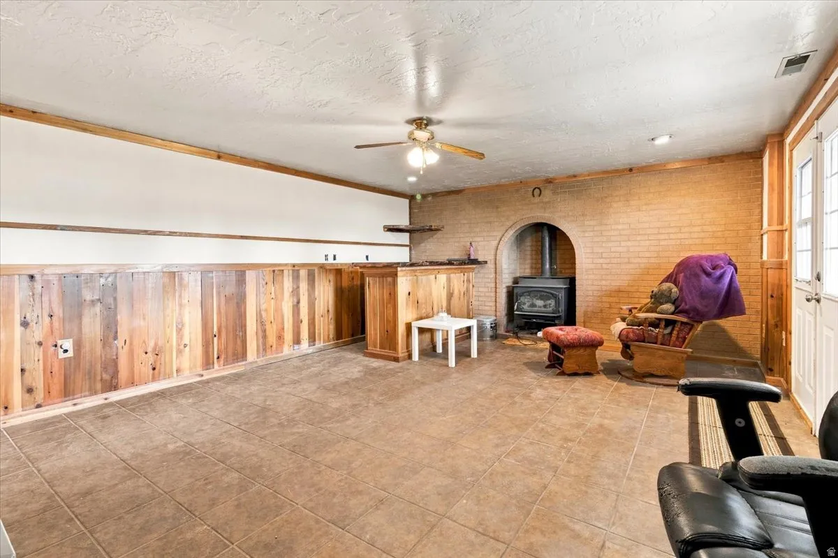 Tile flooring, wood paneling, exposed brick wall, built-in wood-burning stove, and ceiling fan