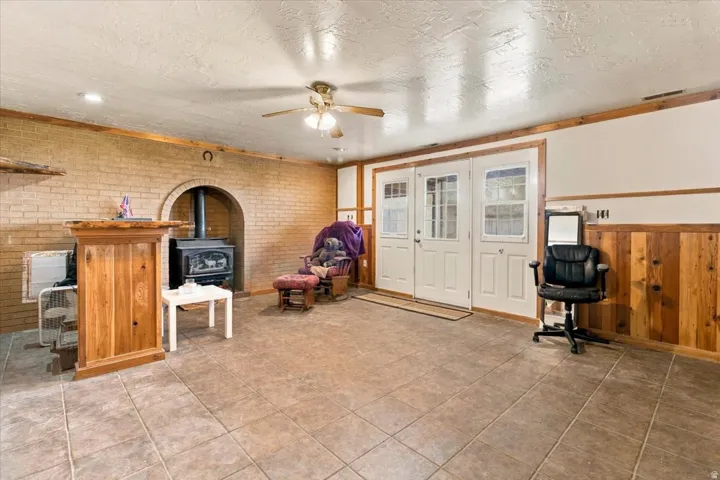 Tiled flooring, brick wall with arched alcove, wood-burning stove, wood paneling, and double French doors with glass inserts