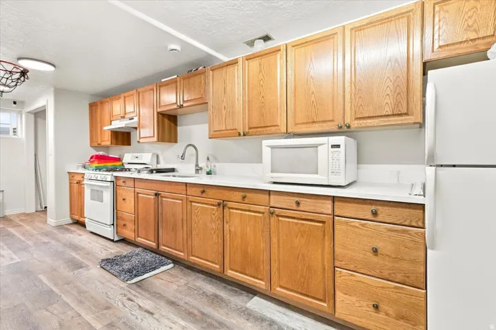 Wood-finish flooring, white countertops, built-in cabinetry, white appliances, and a stainless steel sink with a gooseneck faucet