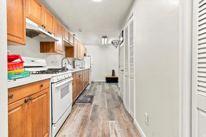 Kitchen featuring wood cabinetry, white countertops, a gas range, and wood-finish flooring