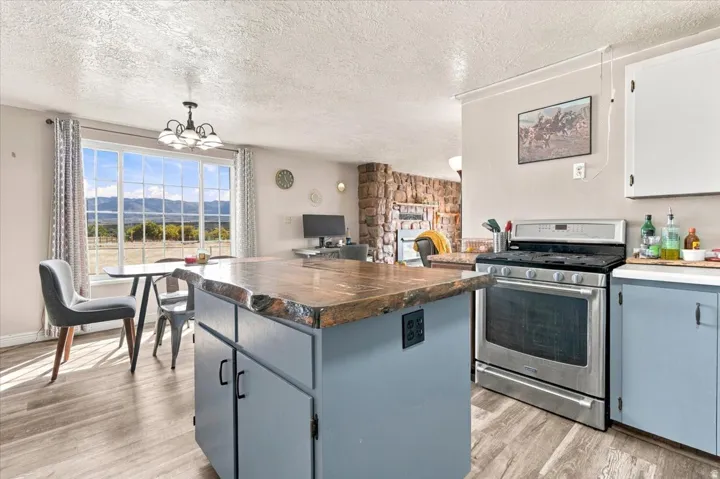 Kitchen island with a natural edge countertop, stainless steel range, light blue cabinetry, and wood-finish flooring