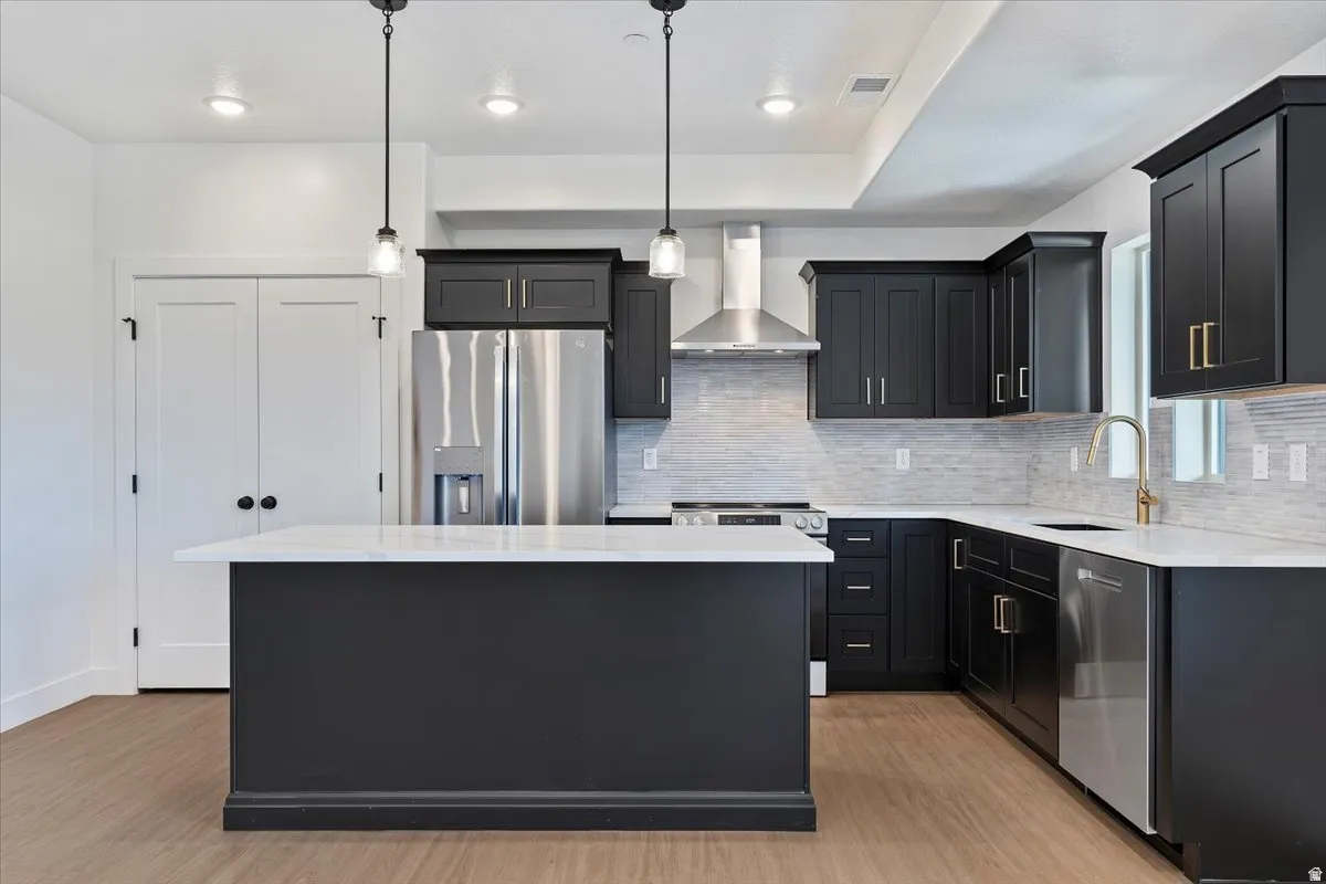 Kitchen featuring dark cabinetry, stainless steel appliances, a center island with a white countertop, recessed lighting, and wood-finish flooring