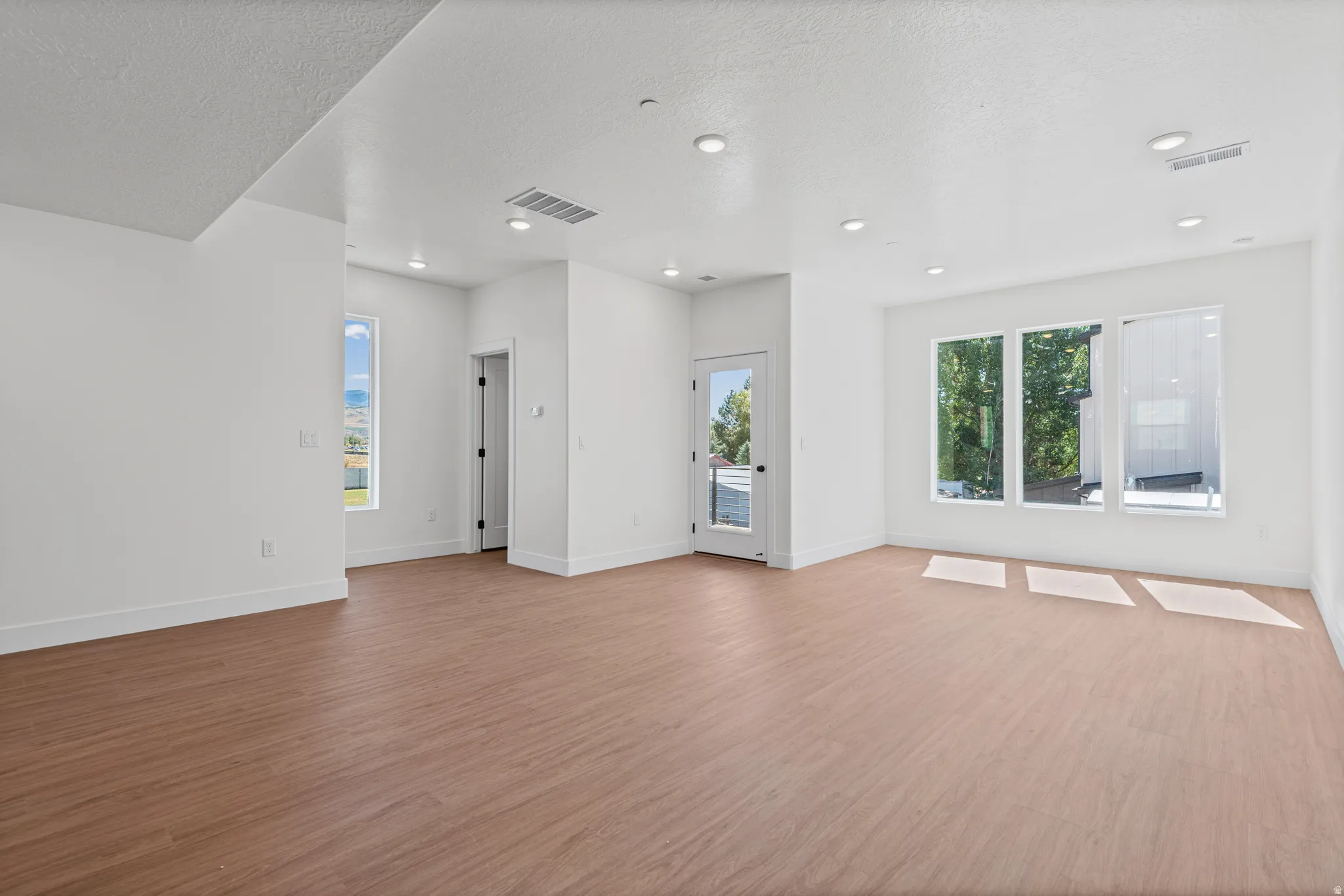 Spacious interior with wood-finish flooring, recessed lighting, multiple windows, and a glass-paneled door