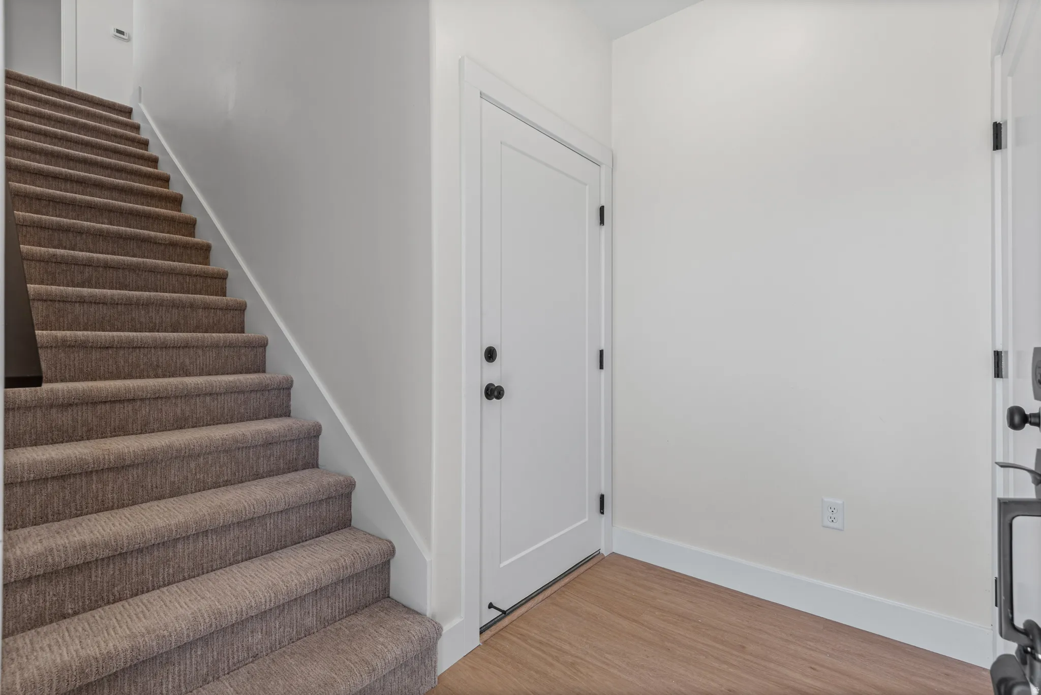 Carpeted staircase, wood-finish flooring, white walls, white doors, and black door hardware