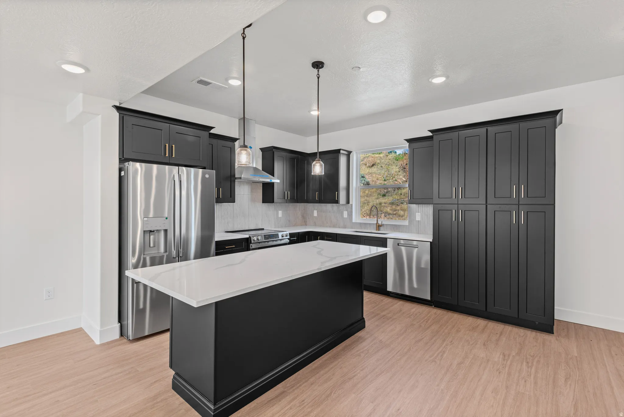 Kitchen featuring dark cabinetry, stainless steel appliances, a center island with a light-colored countertop, recessed lighting, and pendant lights