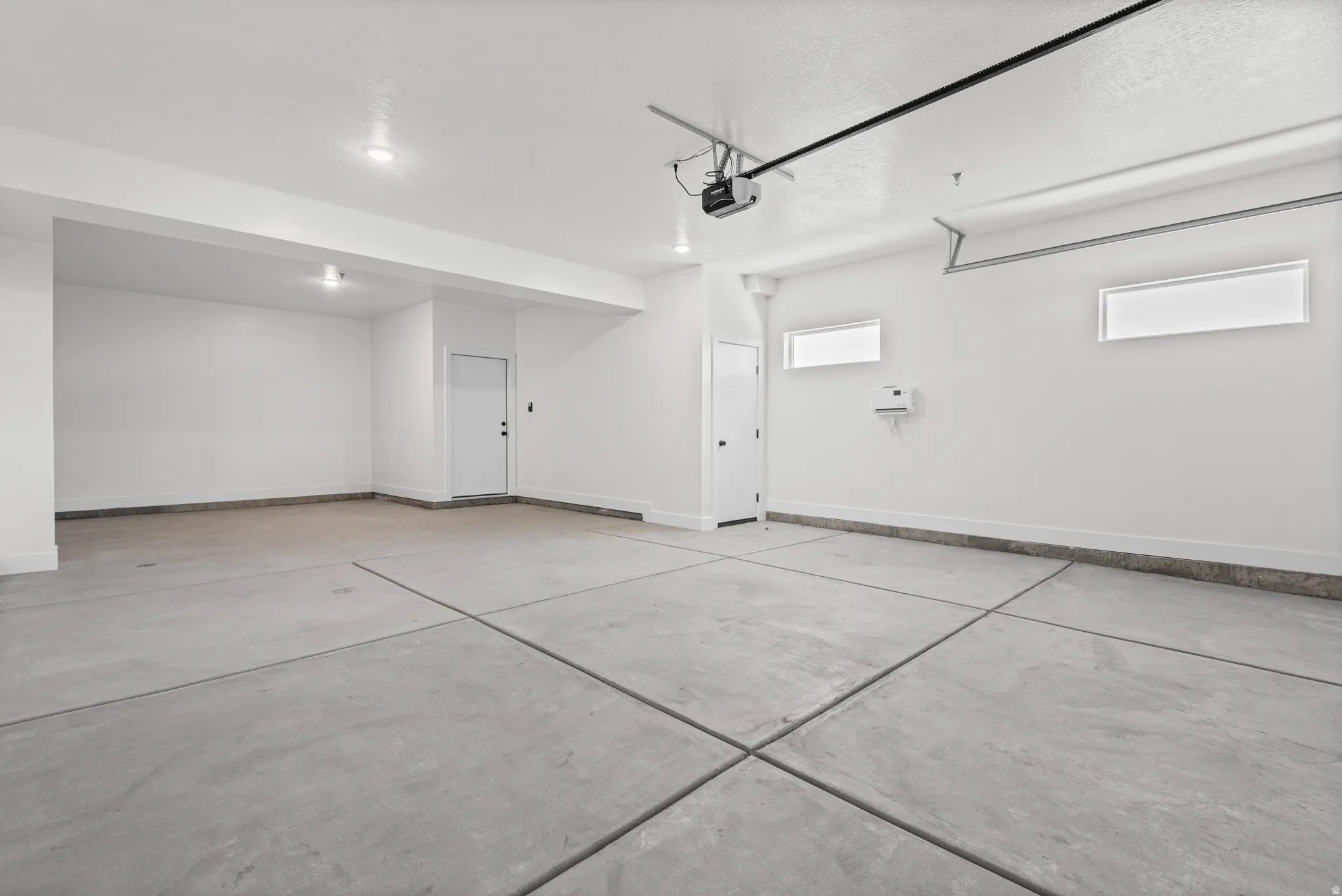 Clean concrete flooring, bright white walls, recessed ceiling lights, and two horizontal windows