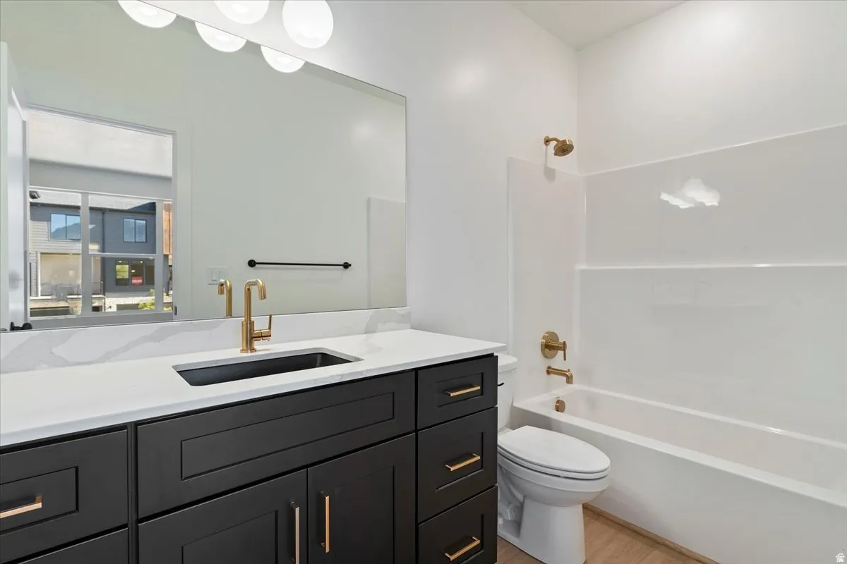 Modern bathroom featuring a dark wood-finish vanity with gold-tone hardware, white countertop, and integrated white tub-shower combination