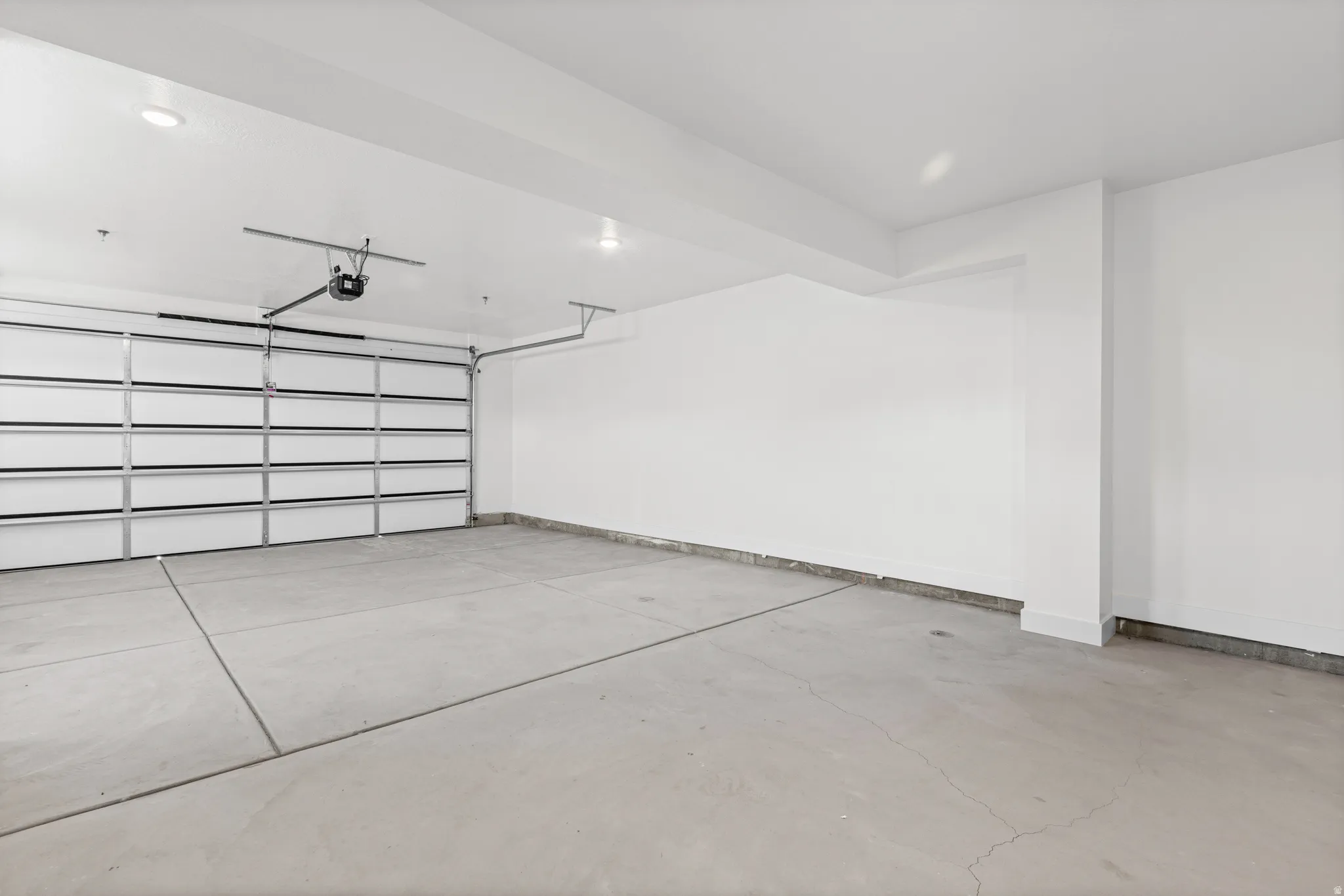 Spacious garage with a concrete floor, overhead door, and white painted walls