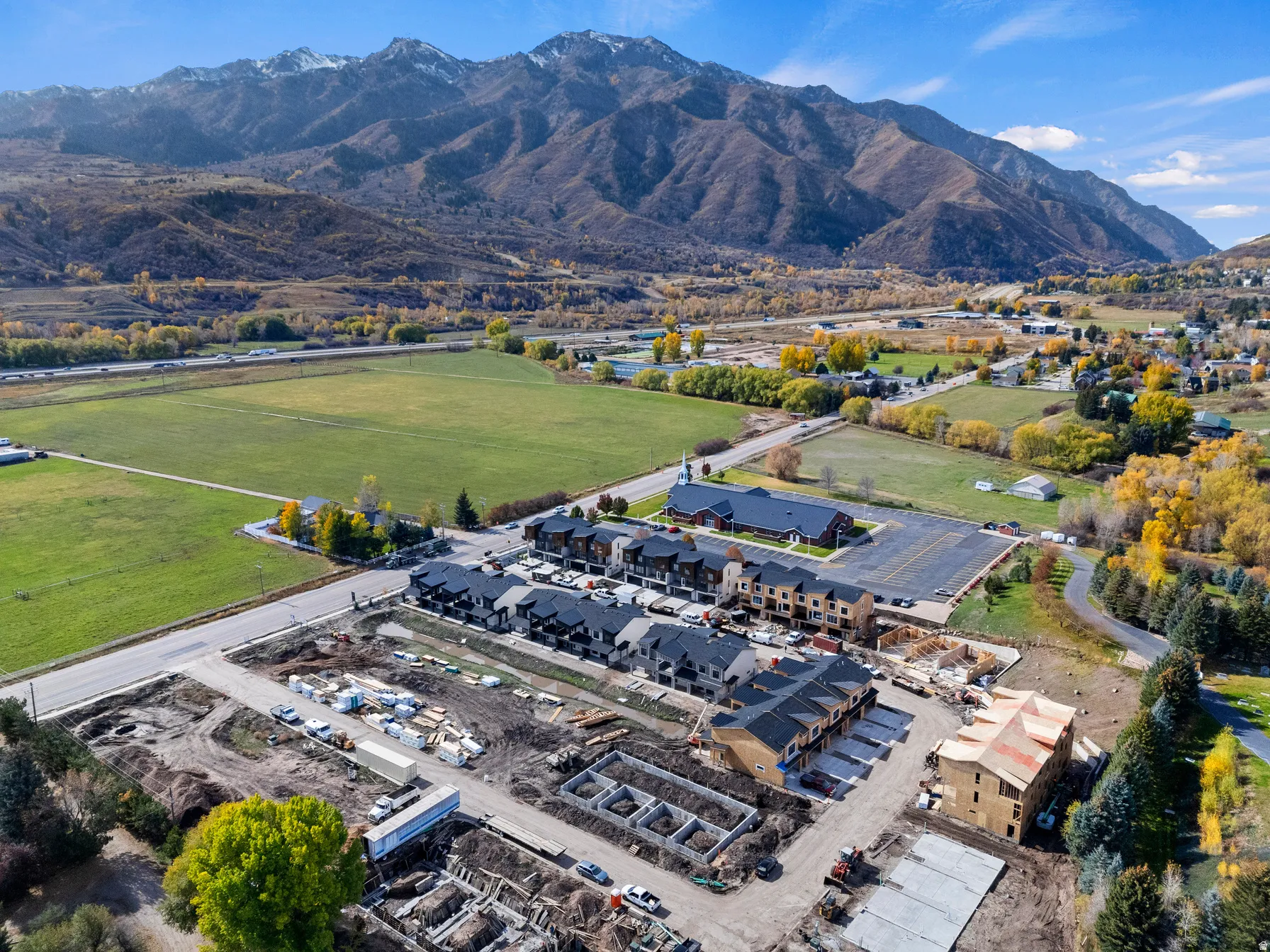 Mountainous backdrop, surrounding green fields, road infrastructure, adjacent residential buildings, and ongoing construction