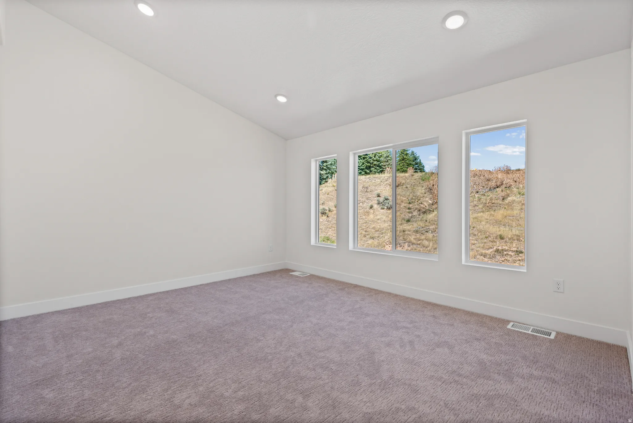 Vaulted ceiling with recessed lighting, three large windows, and neutral carpeting