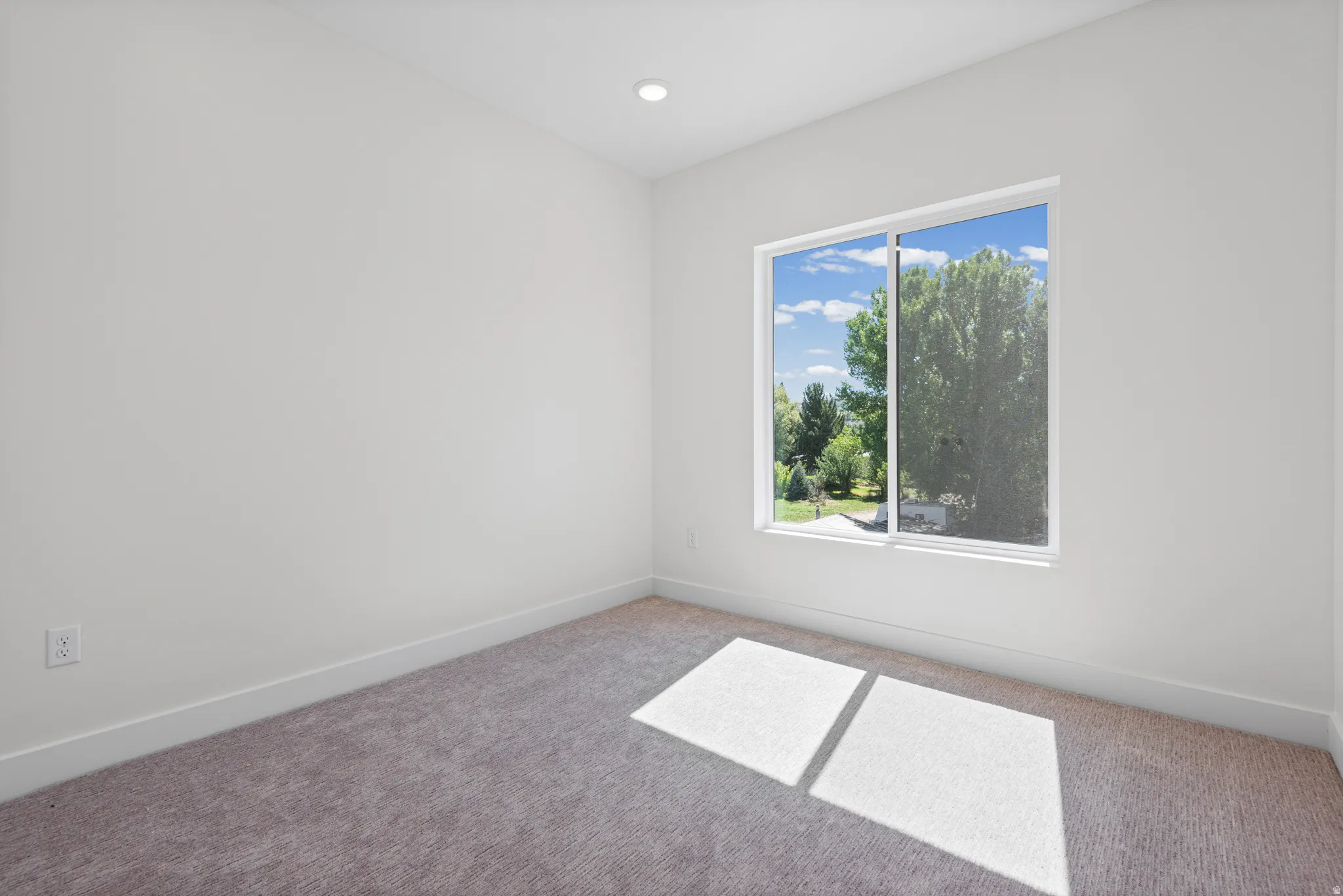 Recessed ceiling lighting, a large window, white walls, and gray carpet