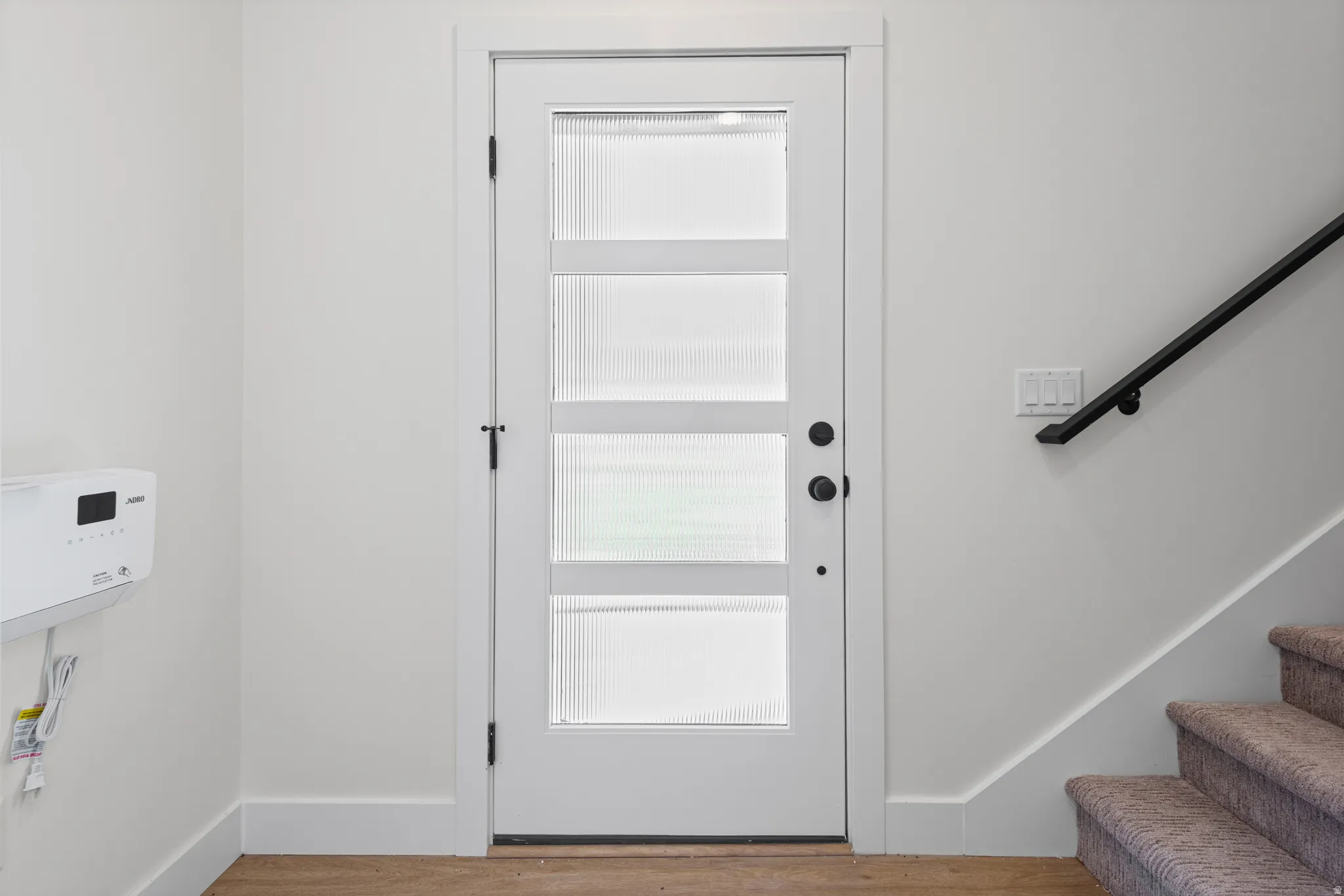 White interior door with four frosted glass panels and matte black hardware, accompanied by a black wall-mounted handrail and a carpeted staircase