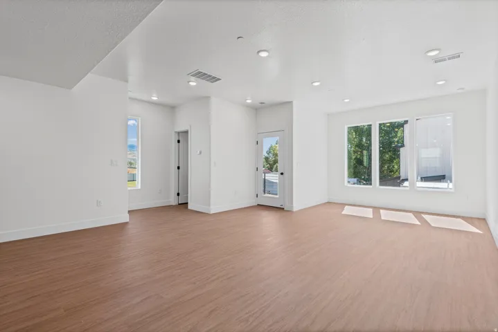 Spacious interior with wood-finish flooring, recessed lighting, multiple windows, and a glass-paneled door