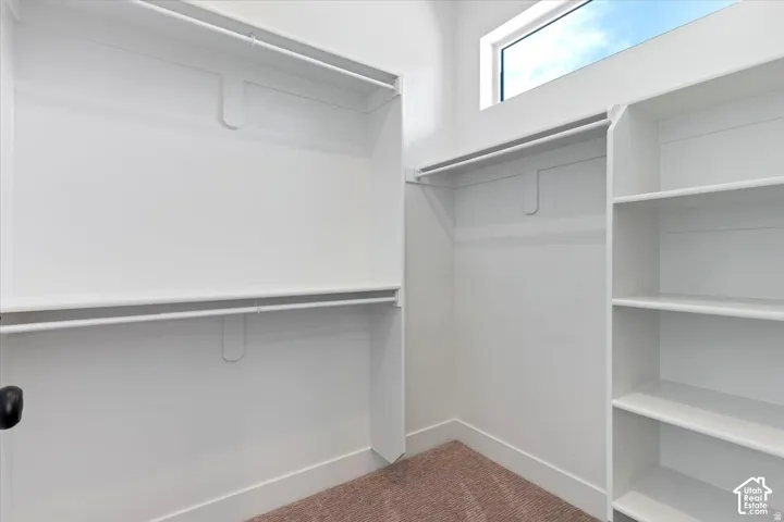 White closet system with multiple hanging rods, built-in shelving, and a high-set window