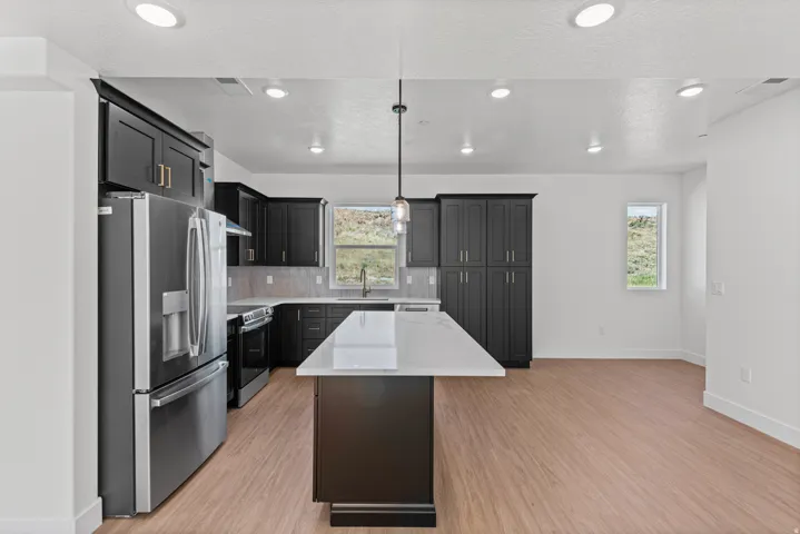 Kitchen featuring dark cabinetry, stainless steel appliances, a center island with a light-toned countertop, wood-finish flooring, and recessed lighting